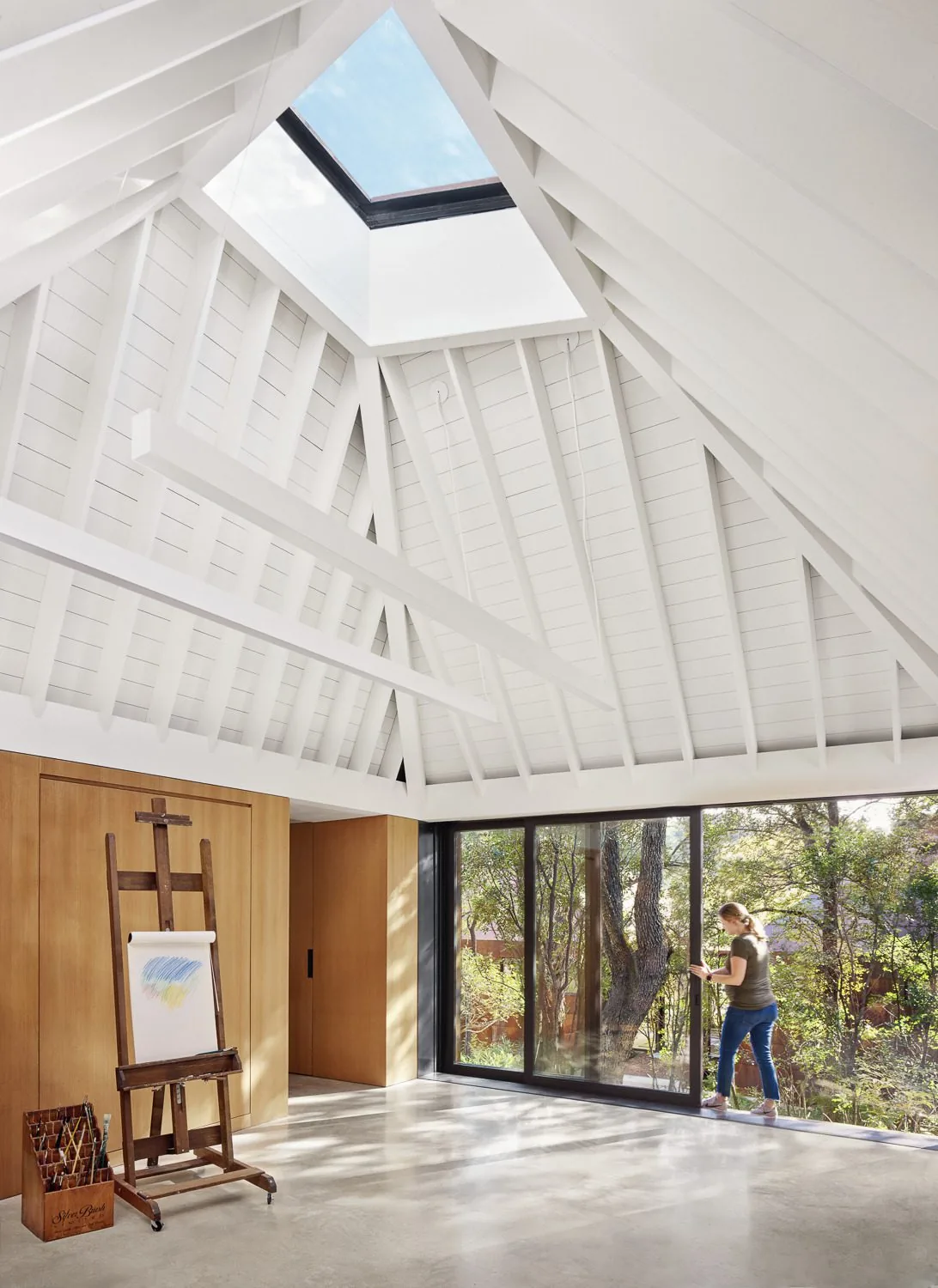 Room features a white vaulted wood strip ceiling with skylight and large sliding glass doors overlooking a wooded yard.