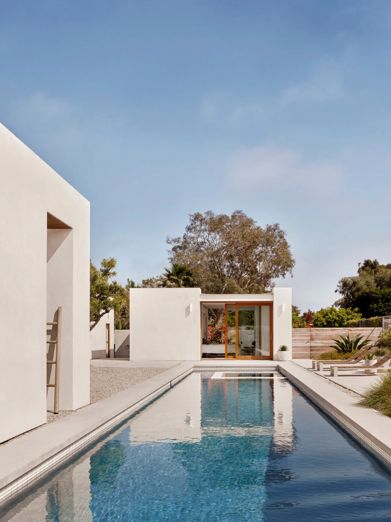 Point Dume Residence features a long pool flanked by minimalist white stucco buildings and landscaping.