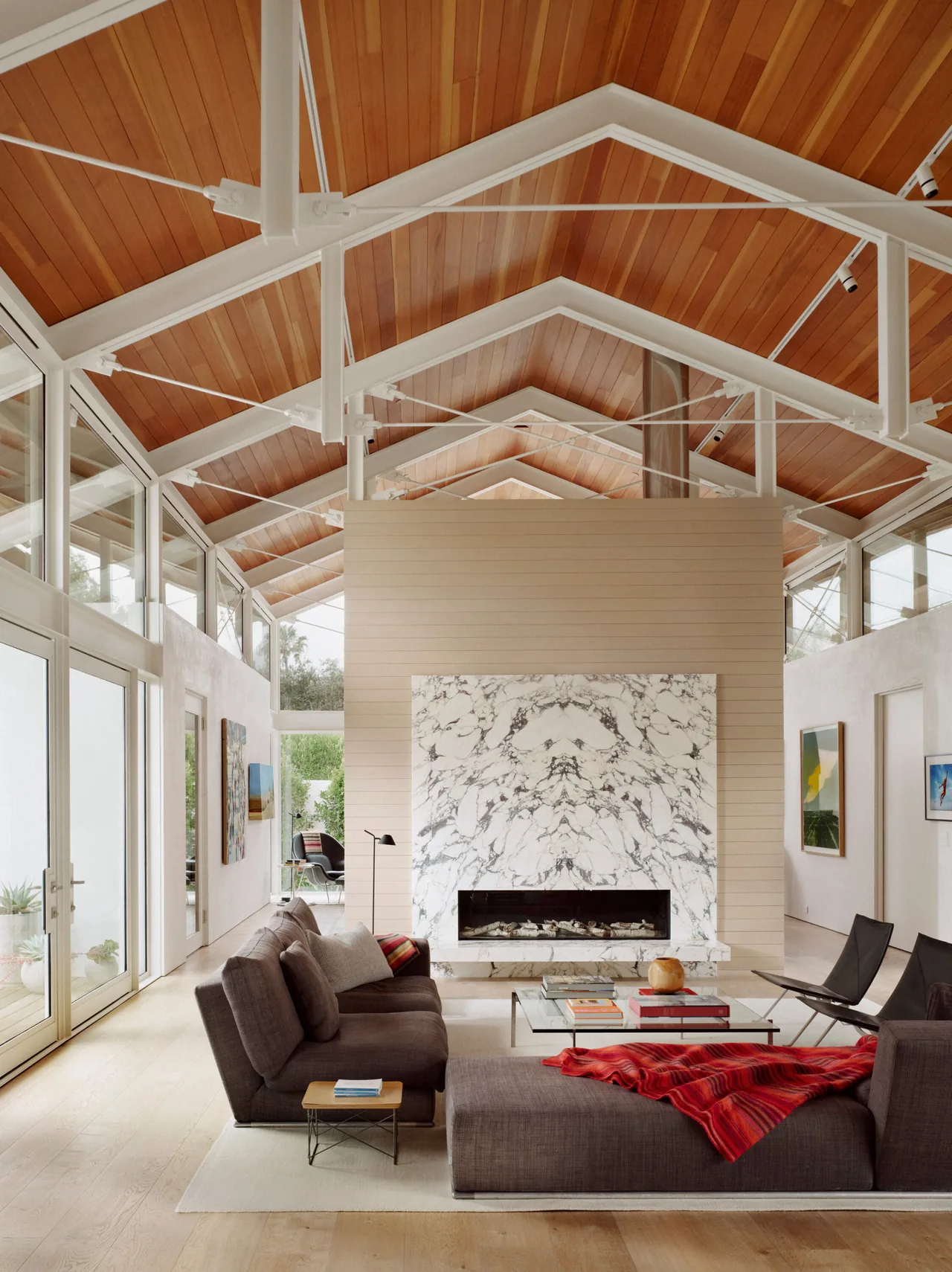 The living room features a vaulted wood ceiling, floor-to-ceiling glass walls, and a marble fireplace at the Point Dume Residence.