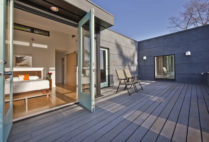 The Mercer Island Remodel features a bedroom opening onto a large outdoor living deck with seating and gray cladding.