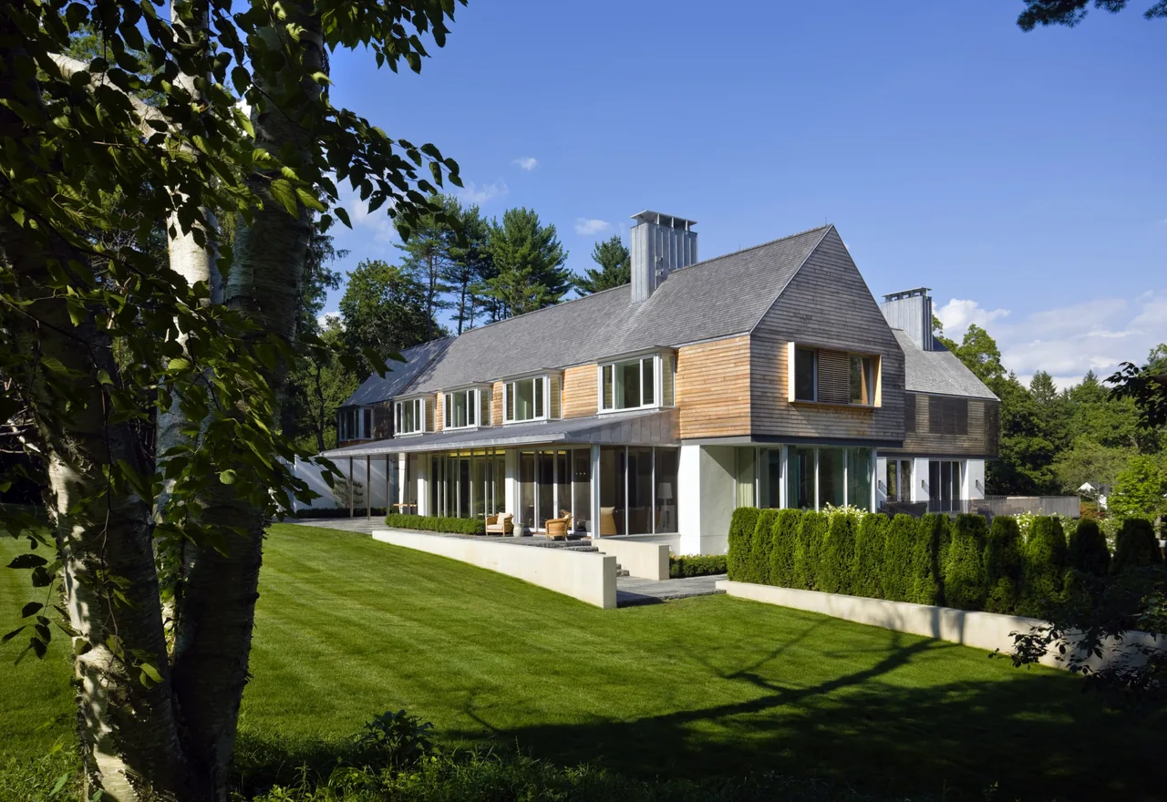 Modern two-story house with wood siding and large windows overlooking a spacious landscaped lawn.