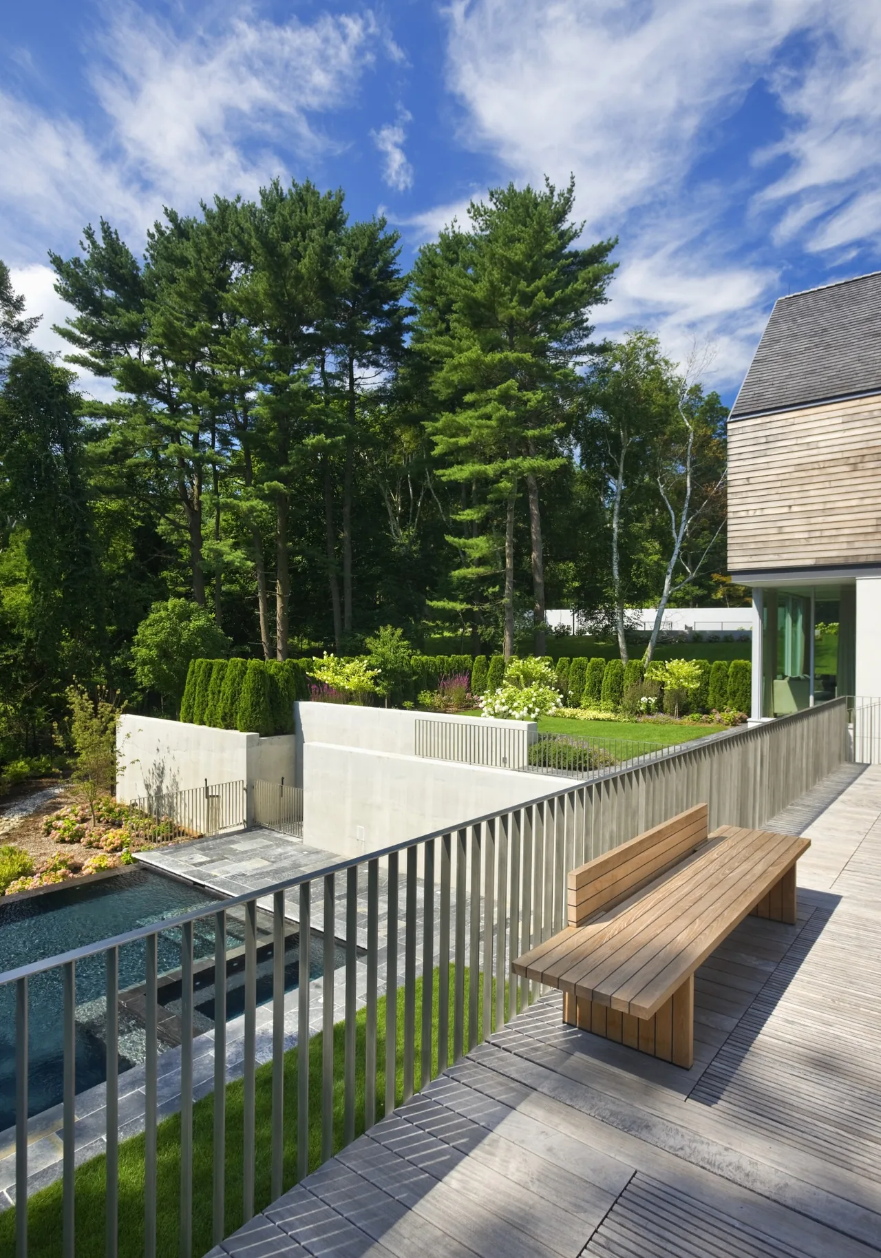 Concrete retaining walls divide a landscaped yard with a wooden bench on a raised patio at project 44PL.