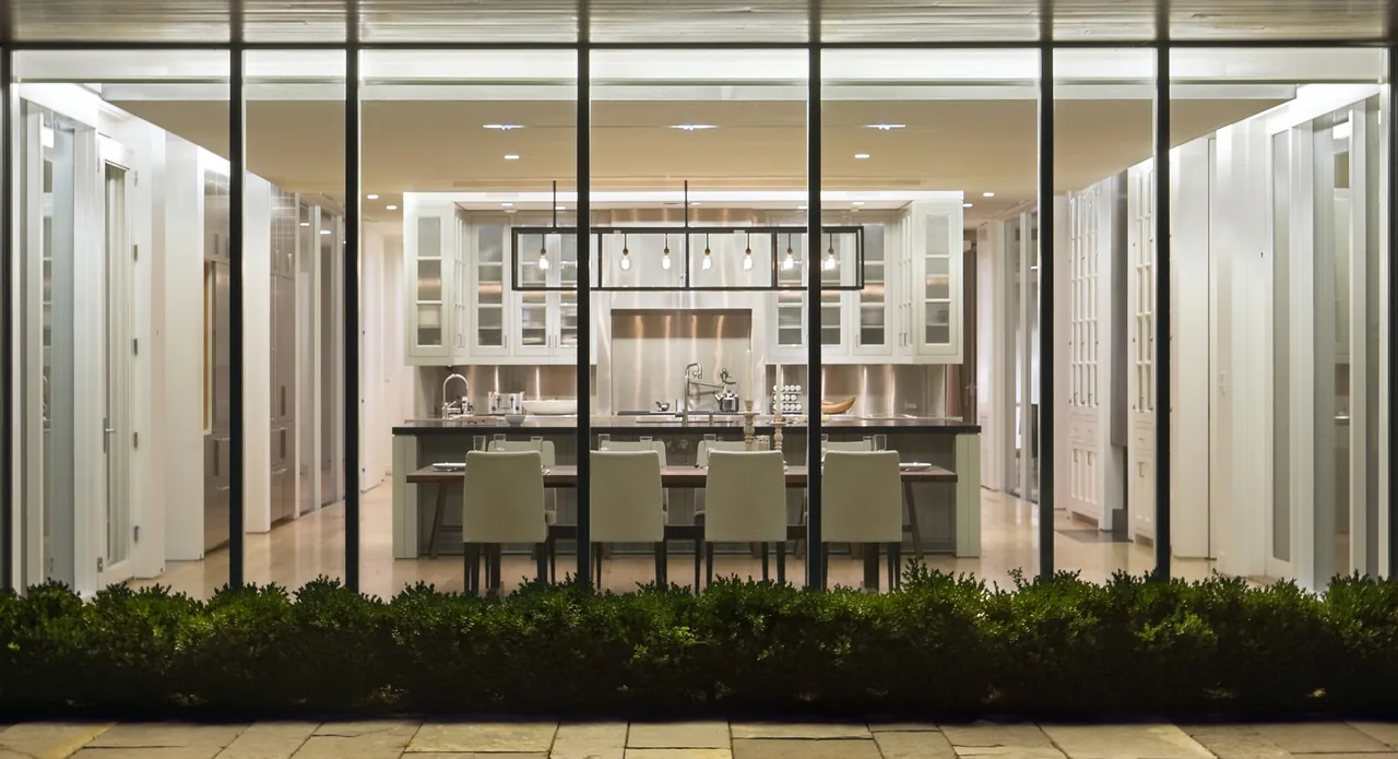 Nighttime view of the kitchen and dining space with floor-to-ceiling glass walls at project 44PL.