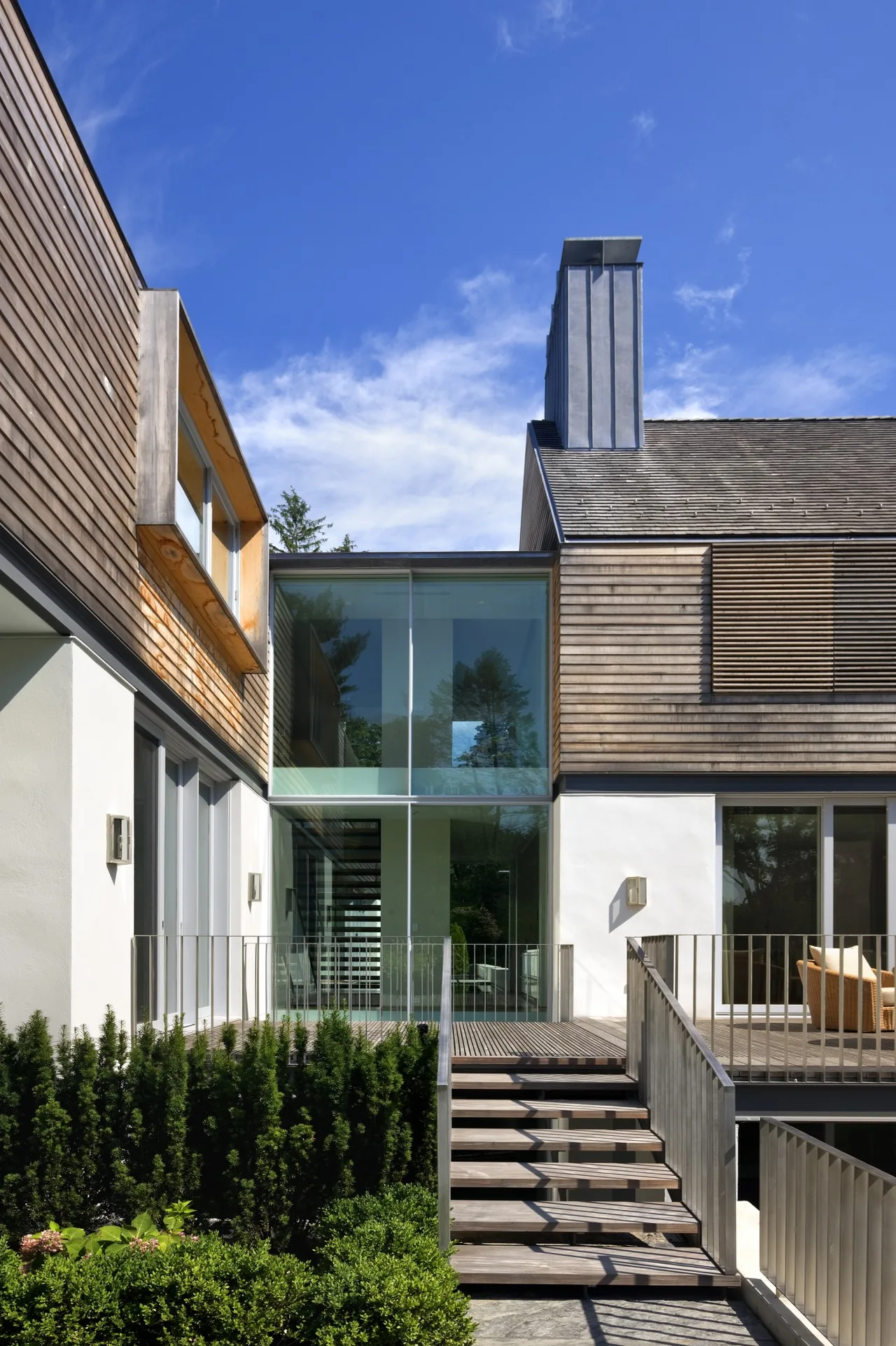 Modern home exterior with slatted wood siding, large glass windows, and a tall metal chimney.