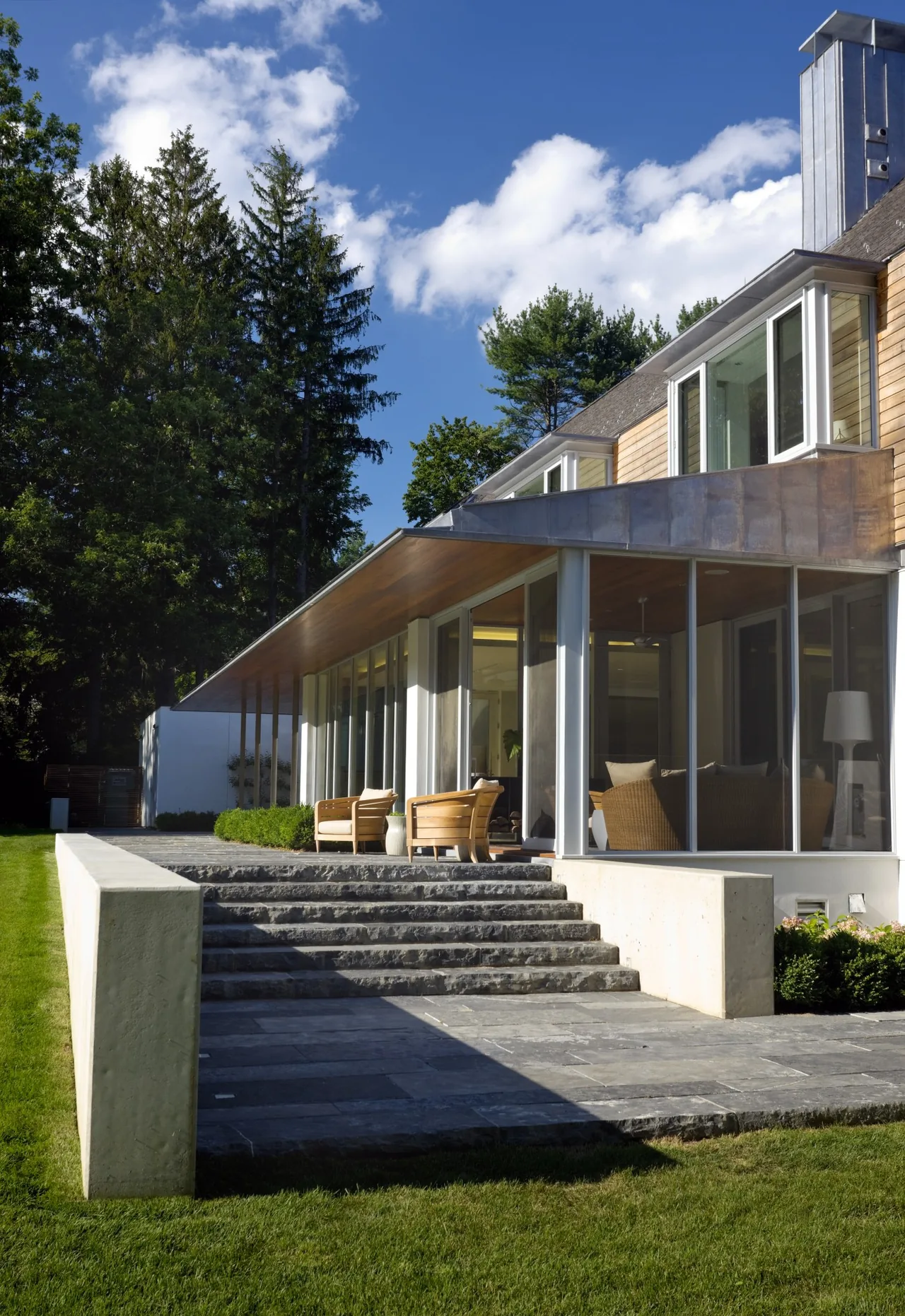The 44PL project features a modern exterior with glass walls, a covered patio, and stone steps in a landscaped lawn setting.