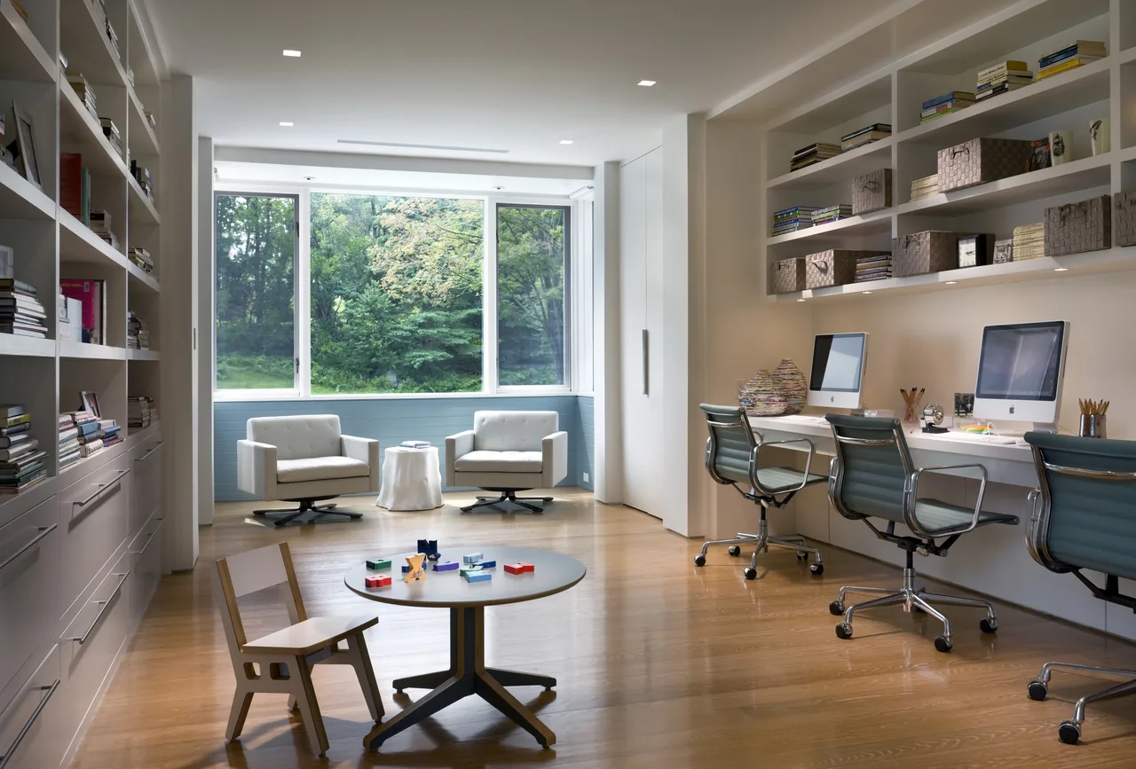 Home office with built-in shelving, two swivel lounge chairs near large window, and a small children's play table with chair.