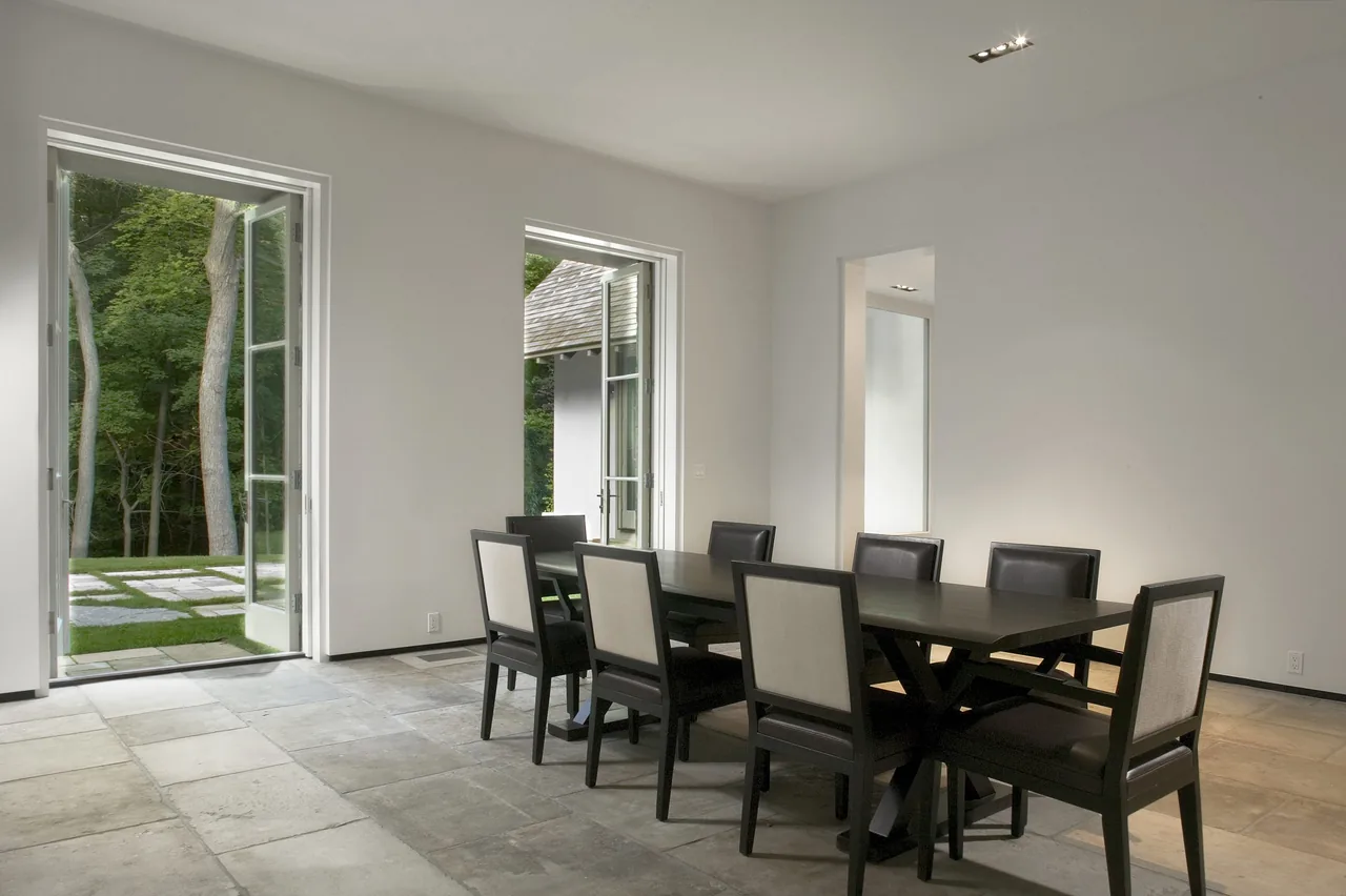 Dining room with black table and chairs features large glass doors opening to a natural stone patio and green landscape.