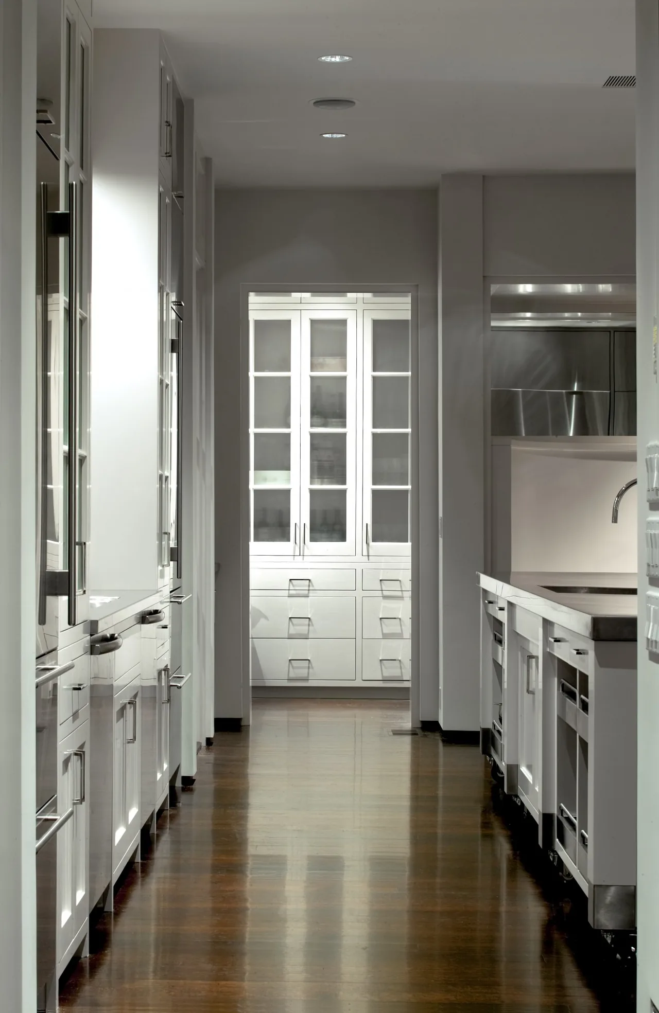 The Riverbank Residence kitchen features white cabinetry with glass fronts and dark hardwood flooring.