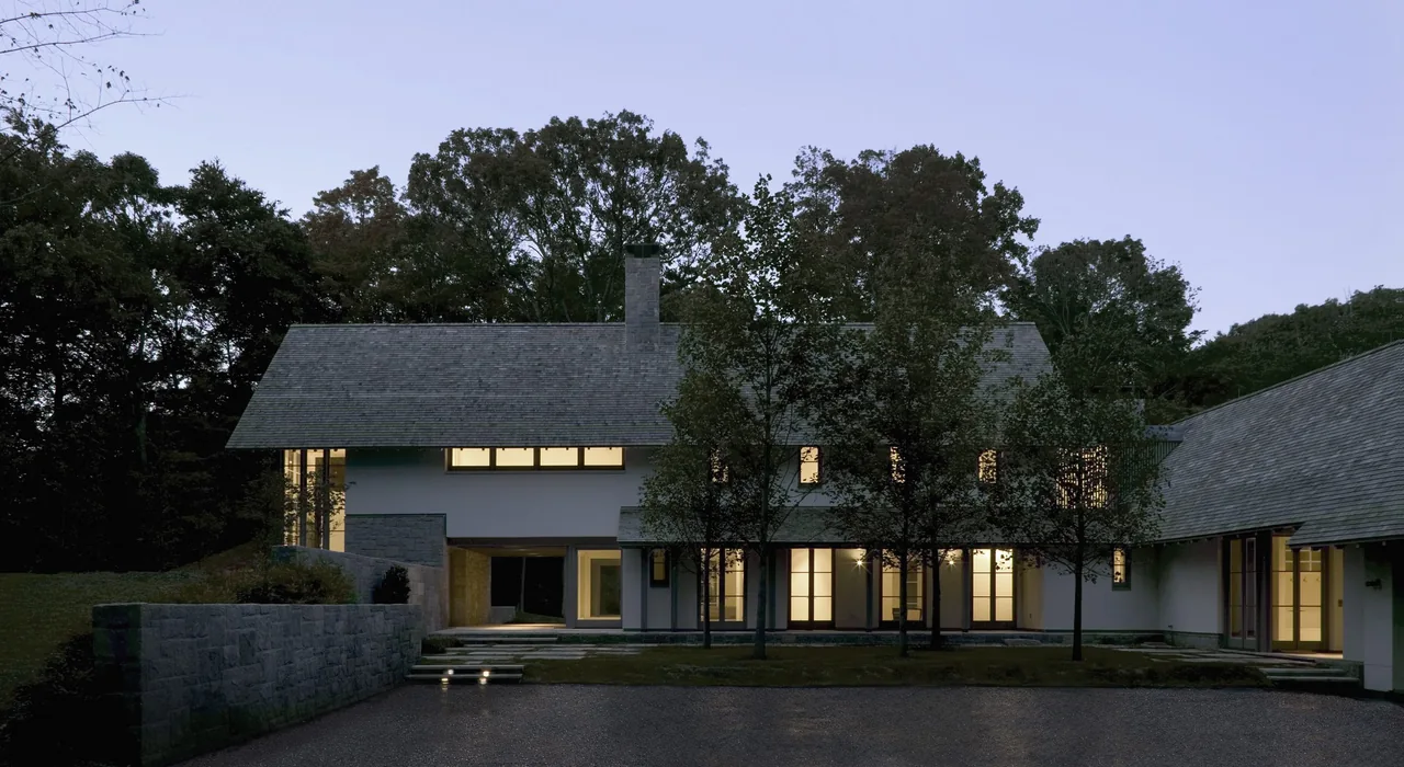 The Riverbank Residence features a modern exterior with large windows and pitched roofs nestled among trees.