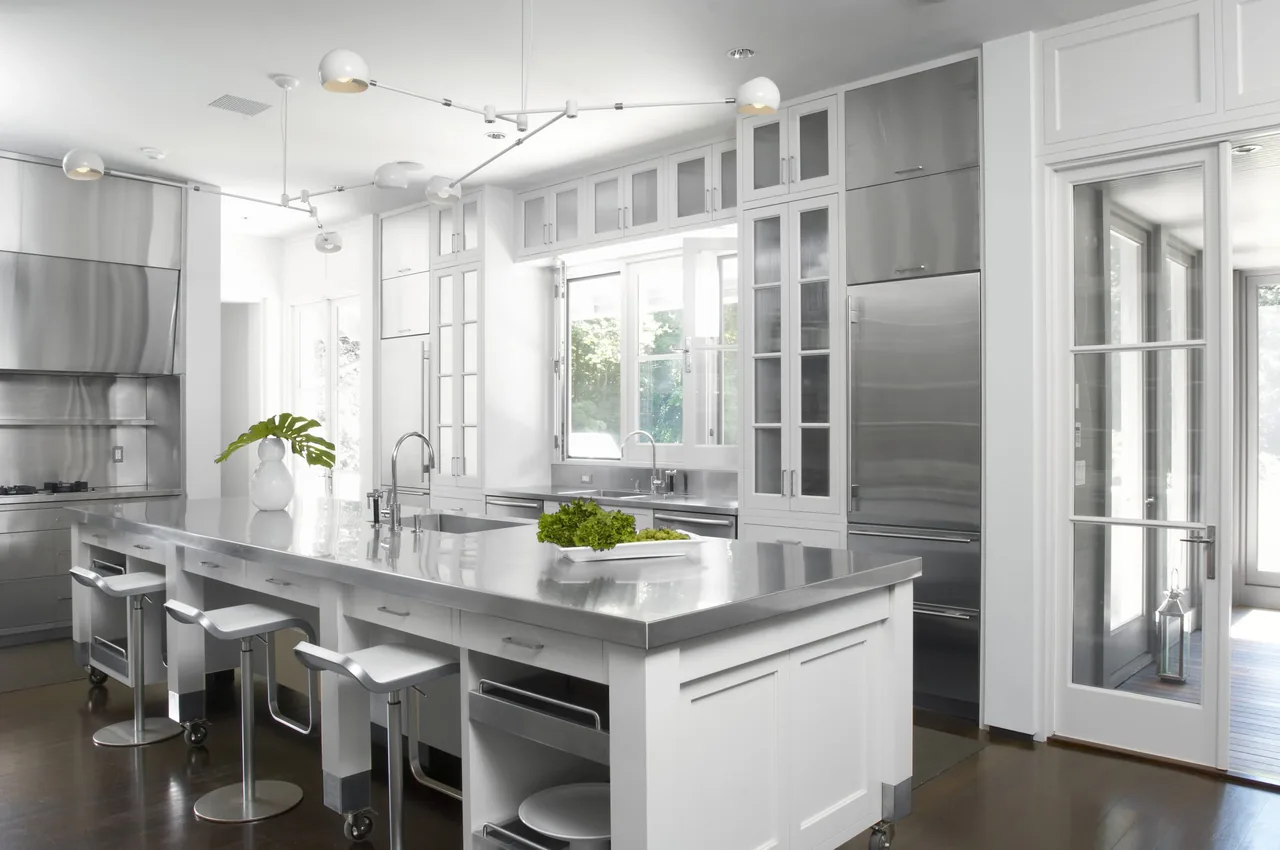 Riverbank Residence kitchen features a large stainless steel island and floor-to-ceiling cabinetry with glass doors.