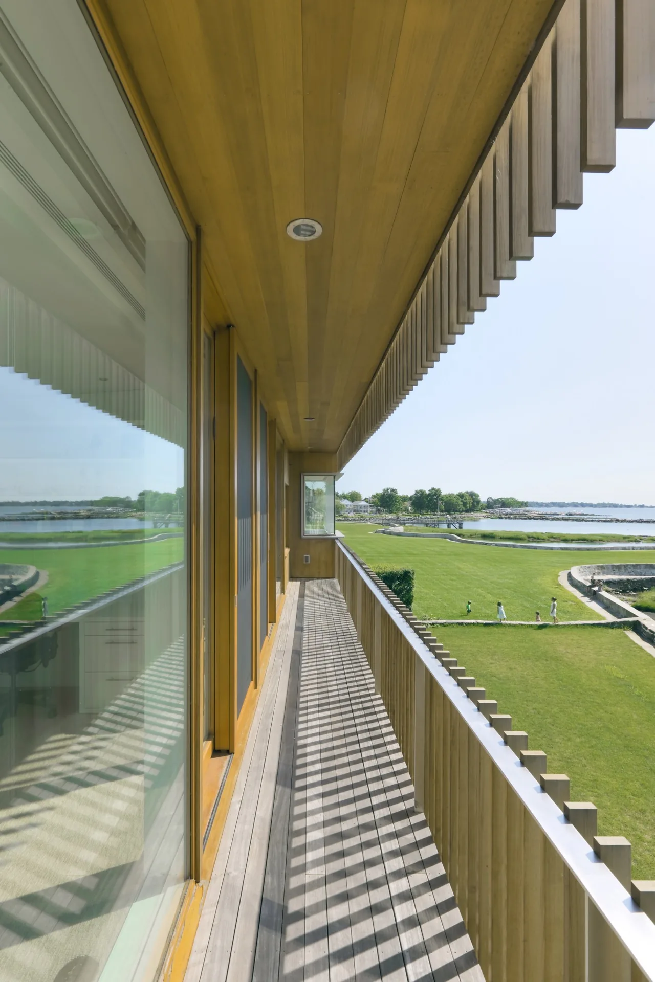 Balcony with vertical wood slat railing and overhang at Spiral House overlooking waterfront and lawn.