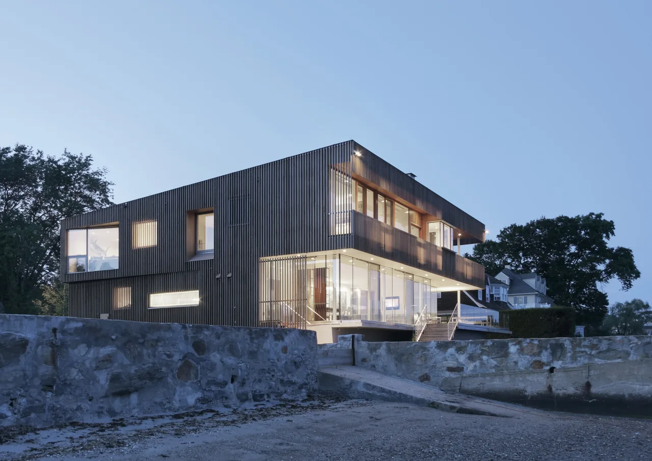 Spiral House features vertical wood slat siding and an elevated two-story design on a rocky foundation.