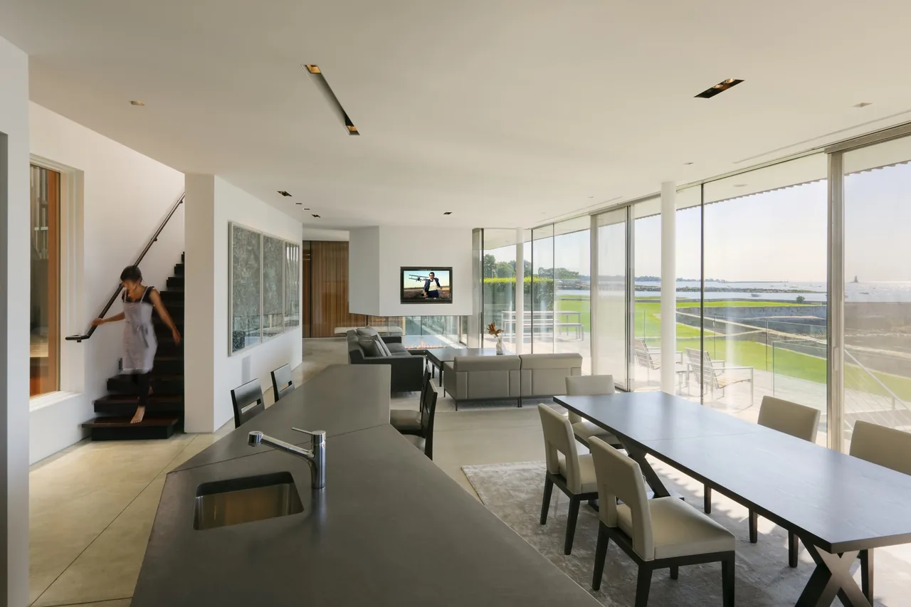 Open living, dining, and kitchen area with expansive glazing overlooking a waterfront landscape.