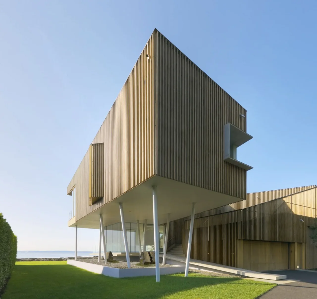 Spiral House features vertical wood siding with an elevated section supported by angled white columns.