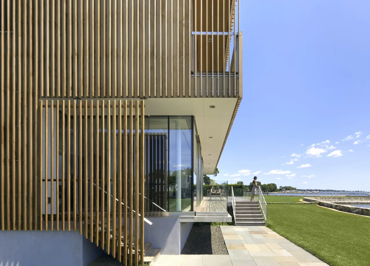 Spiral House features vertical wood slats and floor-to-ceiling glazing on an elevated structure overlooking water.
