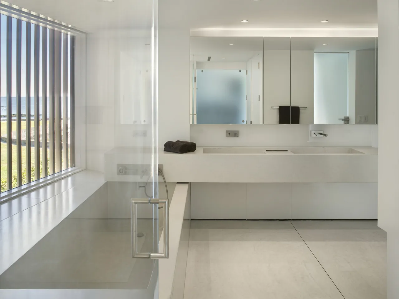 Bathroom featuring a polished concrete tub, large vanity with integrated sink, and vertical wood slats on the window.