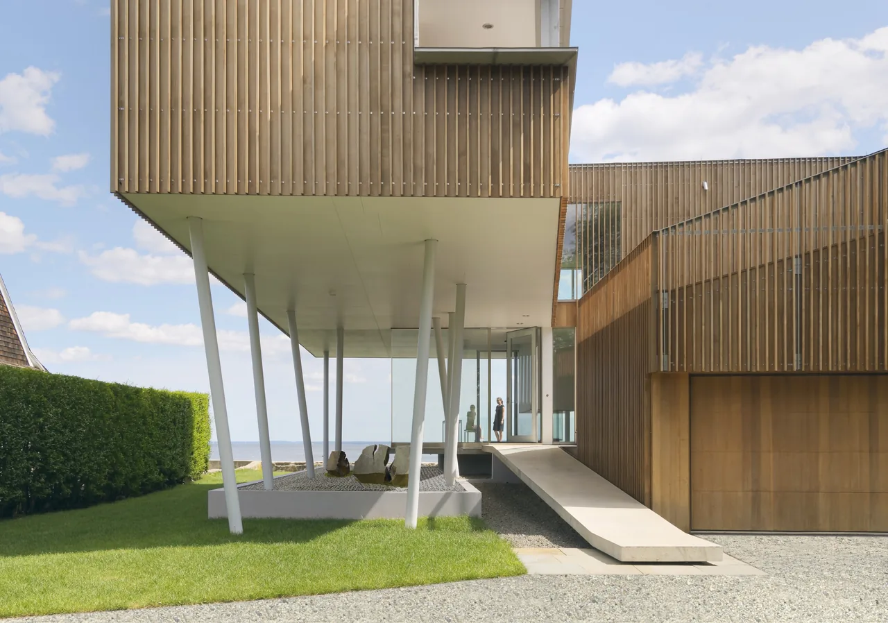 Two-story modern house with elevated structure, angled white supports, and vertical wooden slat siding.