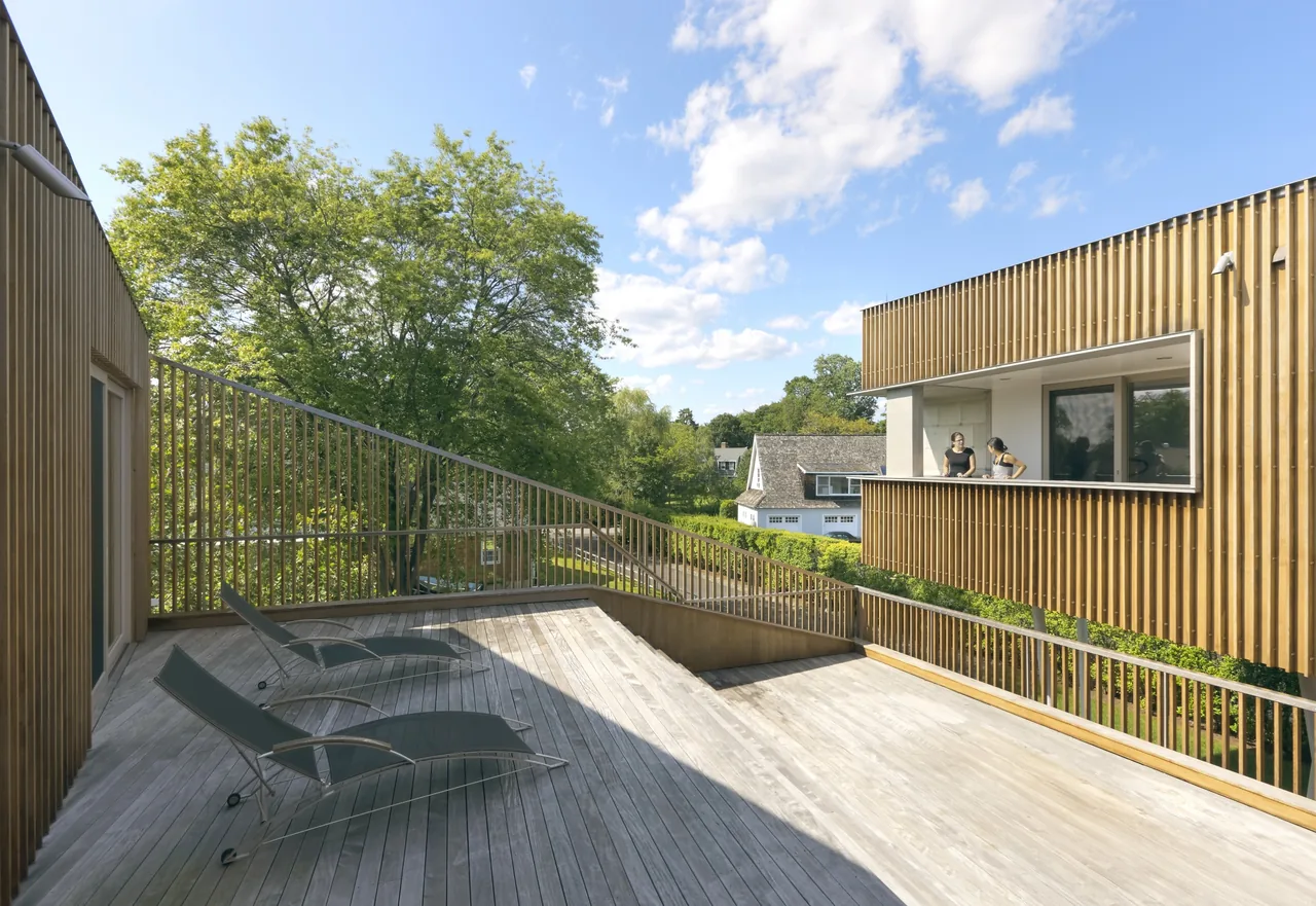 Outdoor deck space featuring vertical wood slat siding on two-story elevated structure with lounge chairs.
