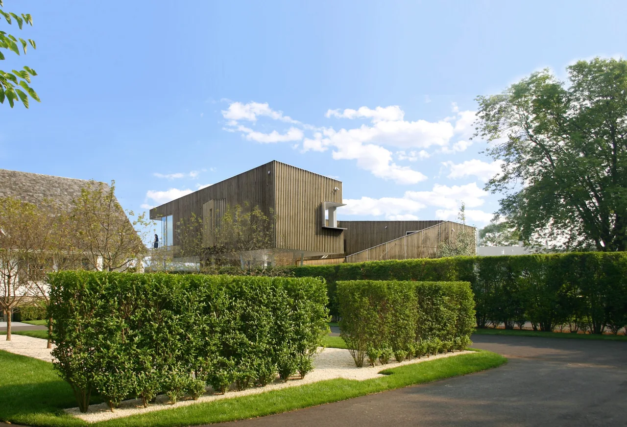 The Spiral House features vertical wood siding and is set amid neatly trimmed hedges and mature trees.