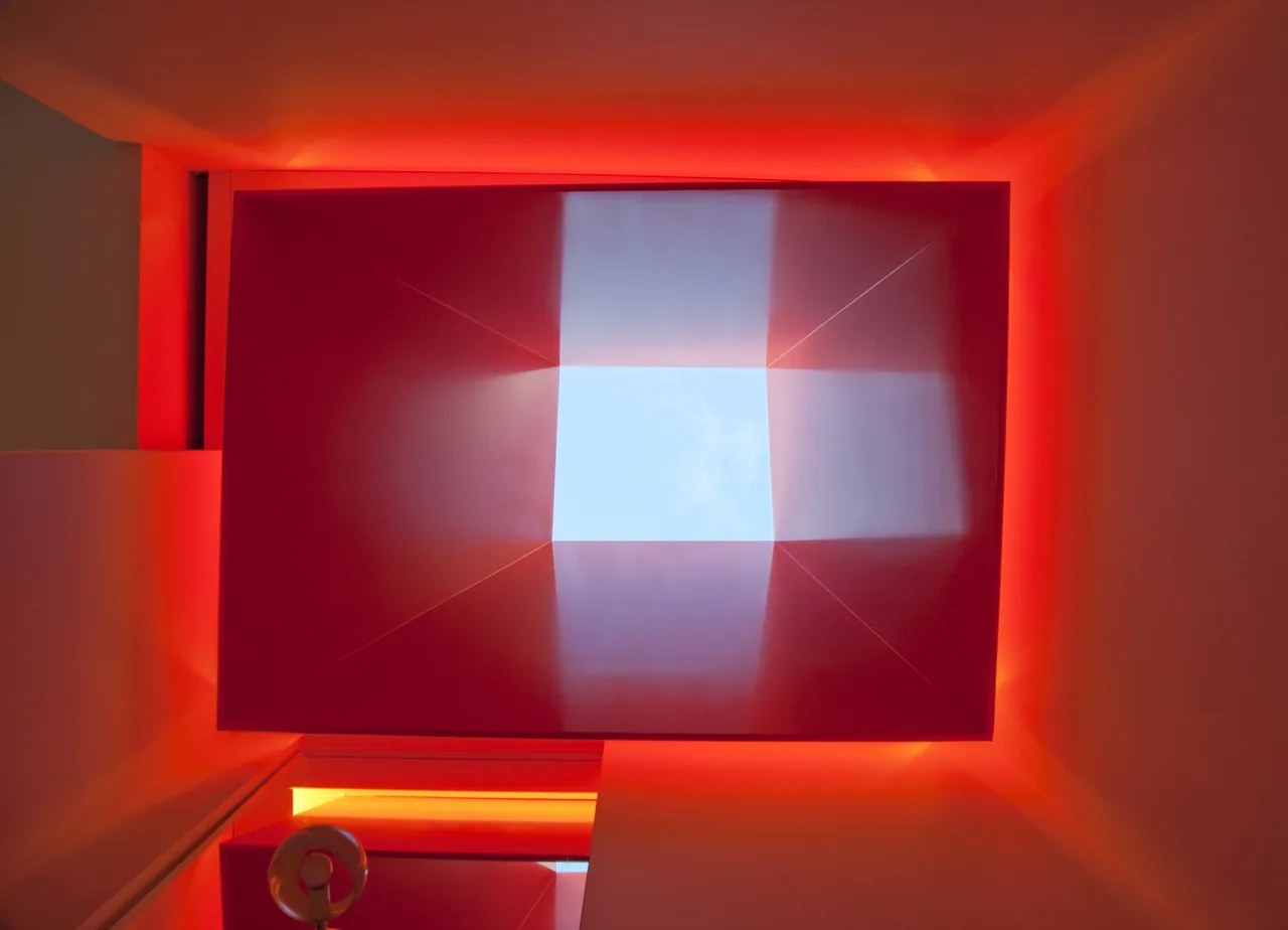 A modern square skylight is set in a ceiling with red ambient lighting around it.