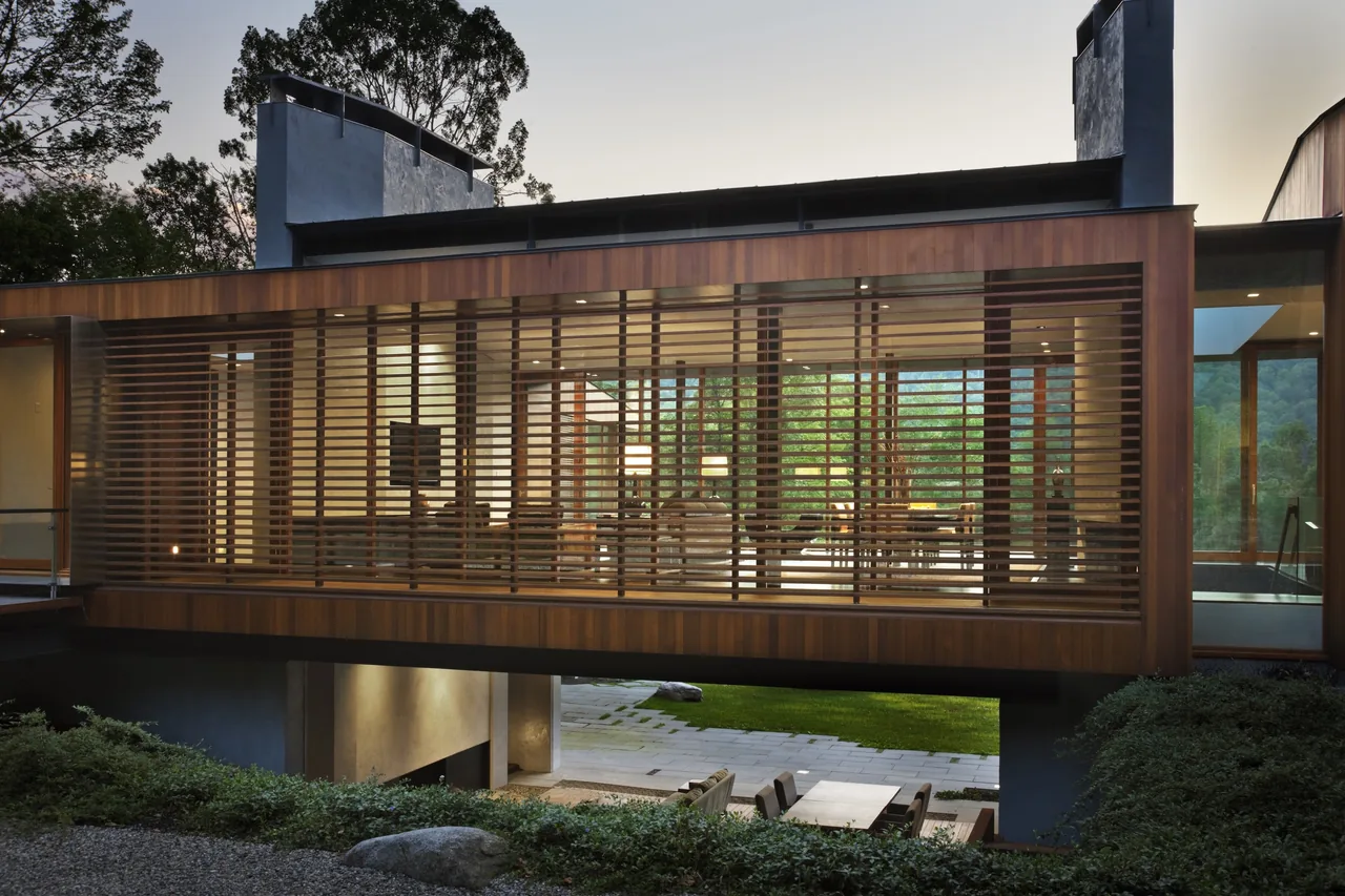 Rear exterior of Bridge House with wood slat screens covering large glazing and outdoor seating below.