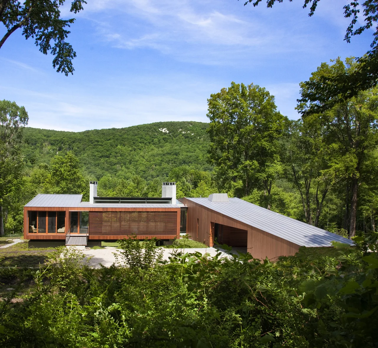 Bridge House by Joeb + Partners, Architects features wood siding and standing seam metal roofs in a forested setting.