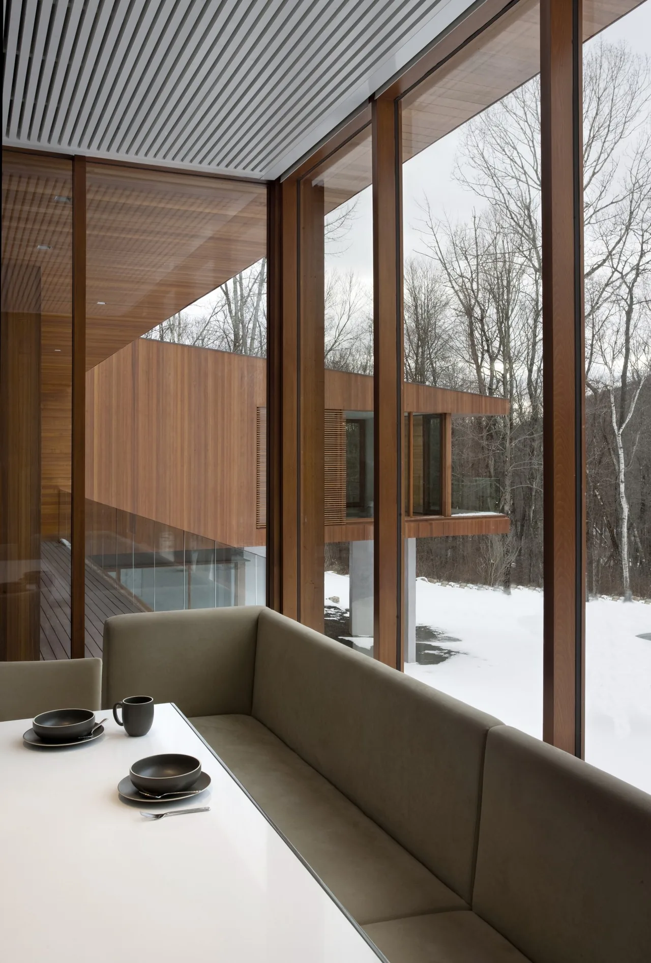 Dining nook features a built-in bench seat and floor-to-ceiling wood-framed windows with views of the snow-covered yard and wood-clad exterior.