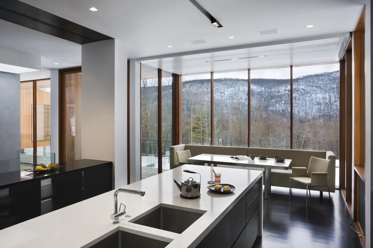 The Bridge House kitchen and dining area feature expansive glazing and minimalist furnishings with mountain views.