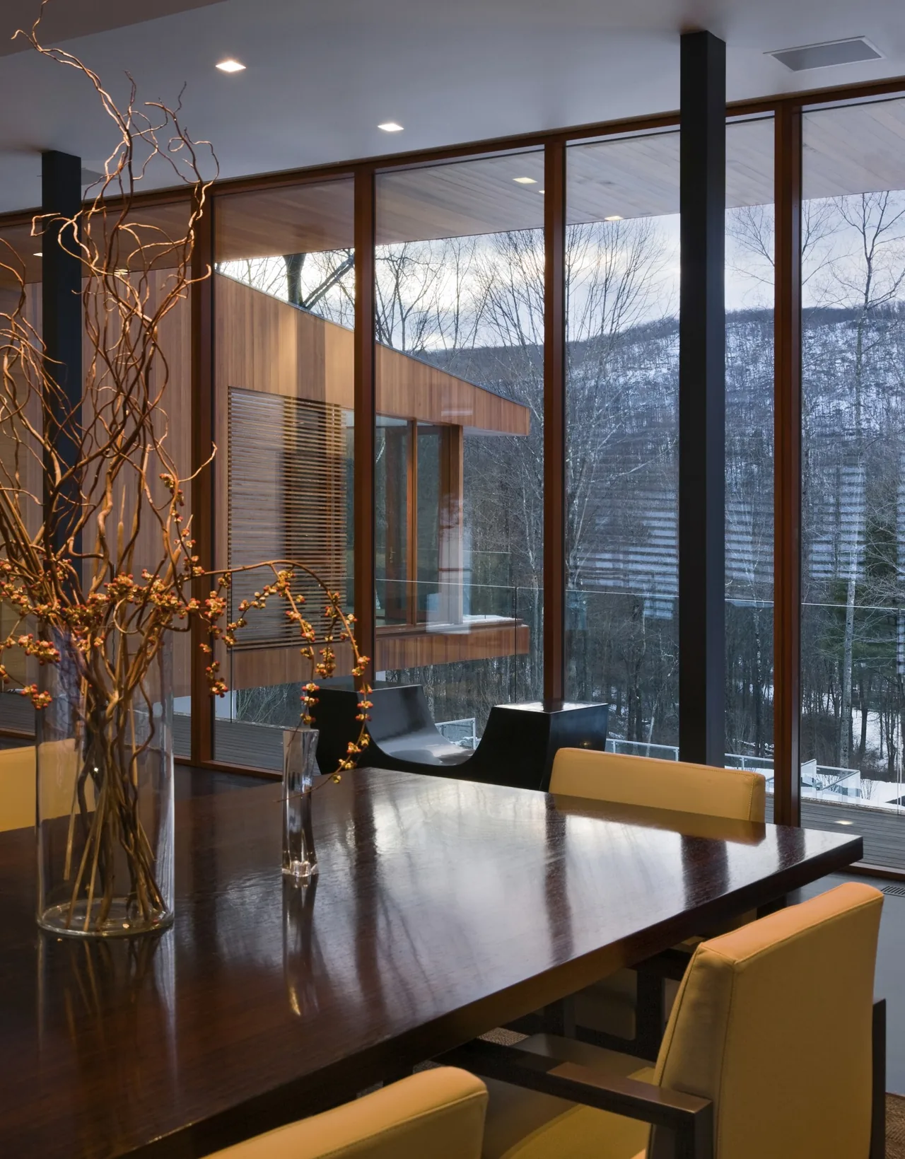 Dining space with dark wood table and floor-to-ceiling wood-framed windows showing snowy mountain views.