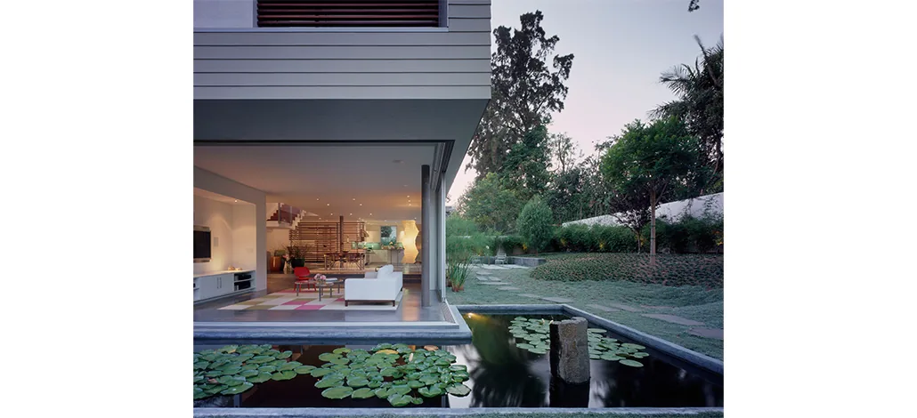 Ehrlich House features an open living room with floor-to-ceiling glass walls opening to a garden with a lily pond visible outside.
