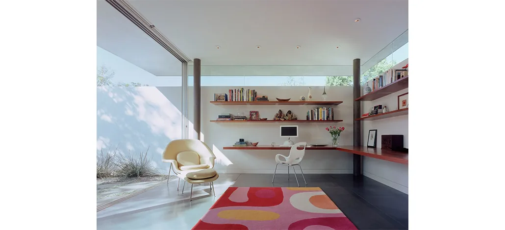 Ehrlich House office features floor-to-ceiling glazing, wood shelving, and a vibrant area rug.