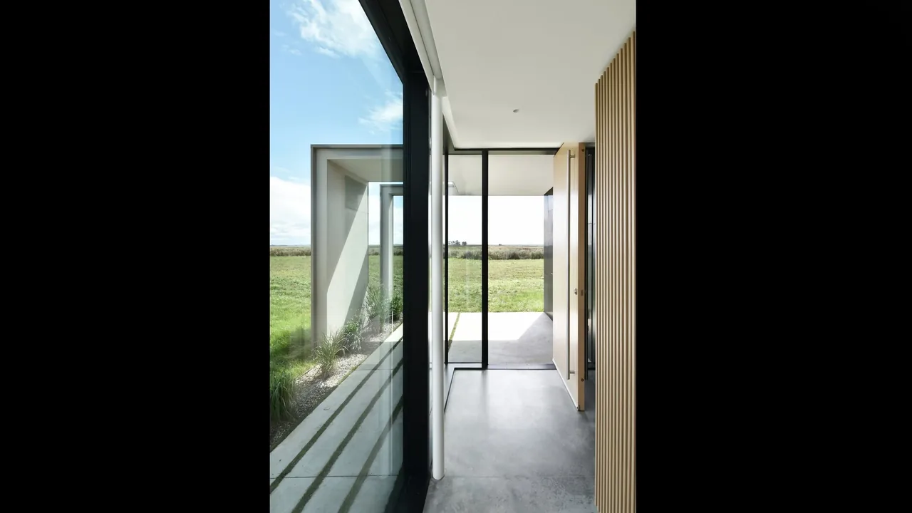 Entry hallway with floor-to-ceiling glazing opens to a landscape view over an open lawn.