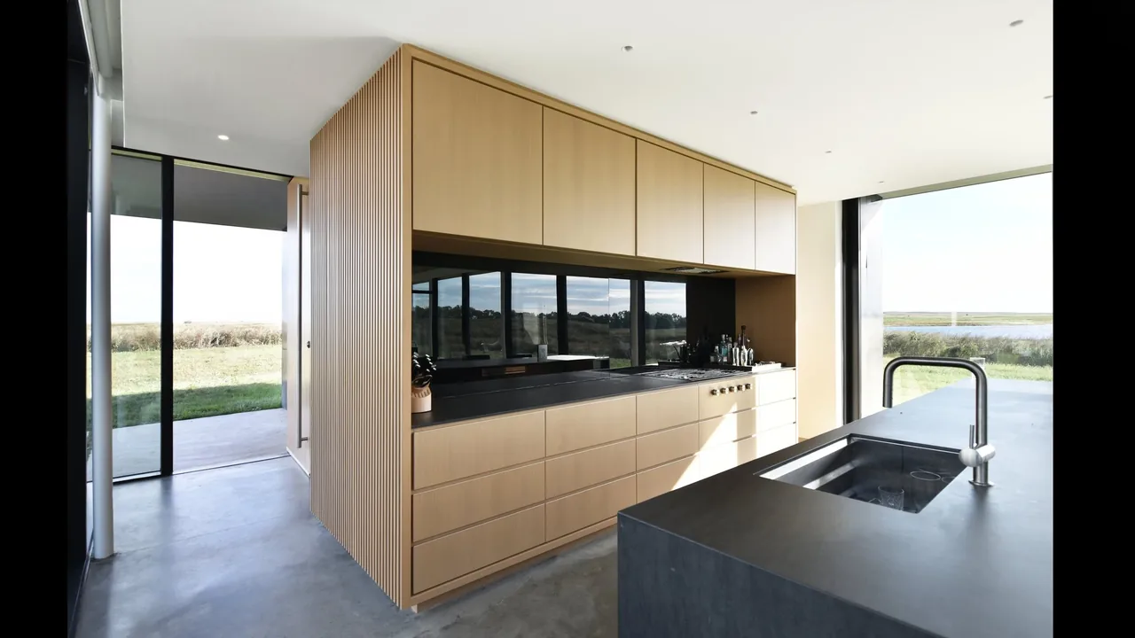 Kitchen with light wood cabinets, black countertops, and large windows facing a waterfront view at Spoonbill Ranch.