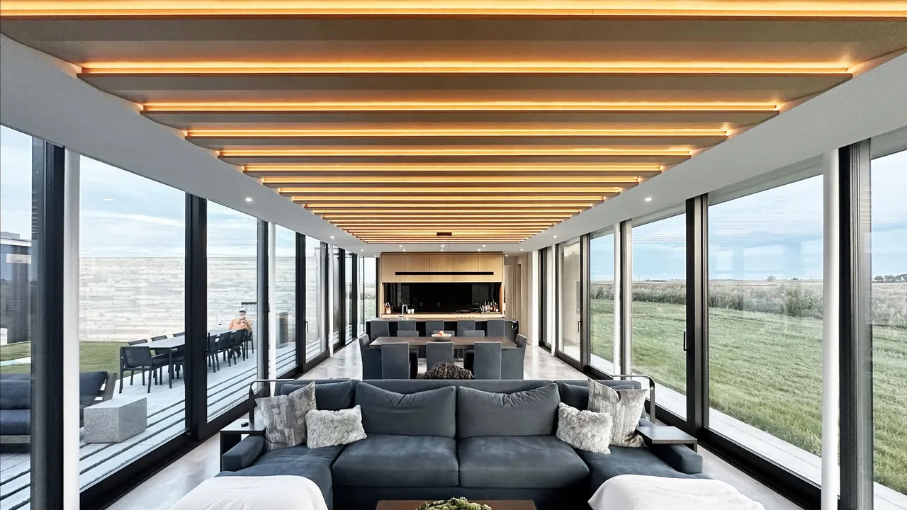 Open living and dining space with large glass walls and illuminated wooden ceiling beams at Spoonbill Ranch.