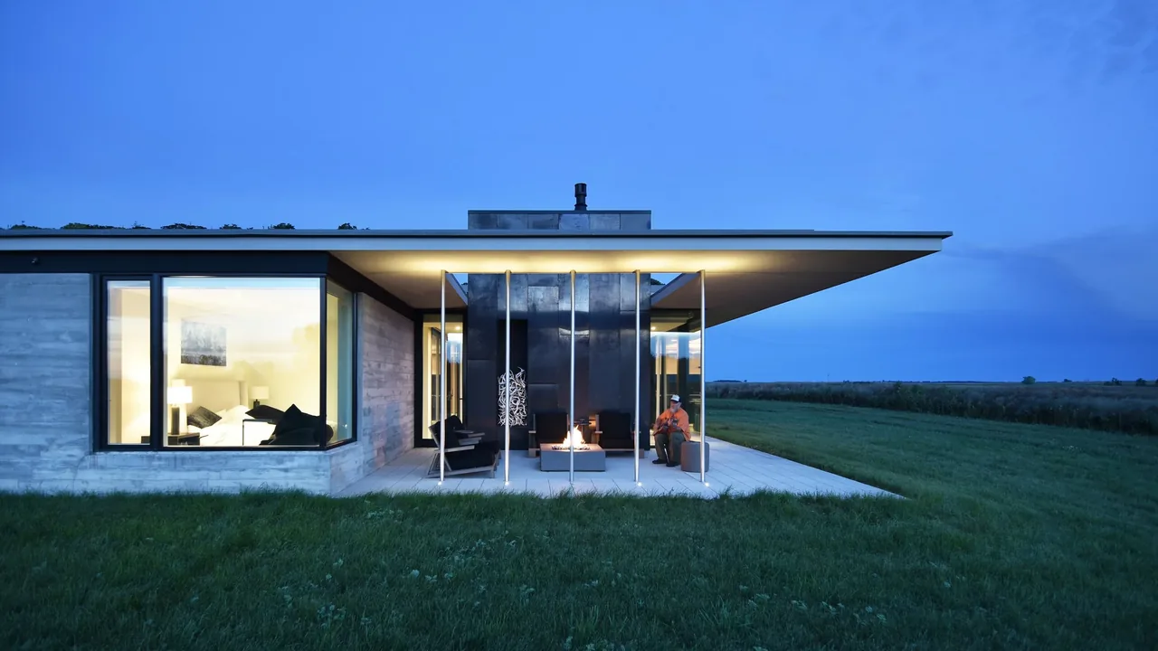 The Spoonbill Ranch features a modern covered patio with outdoor seating and a fire pit overlooking a grassy lawn at dusk.