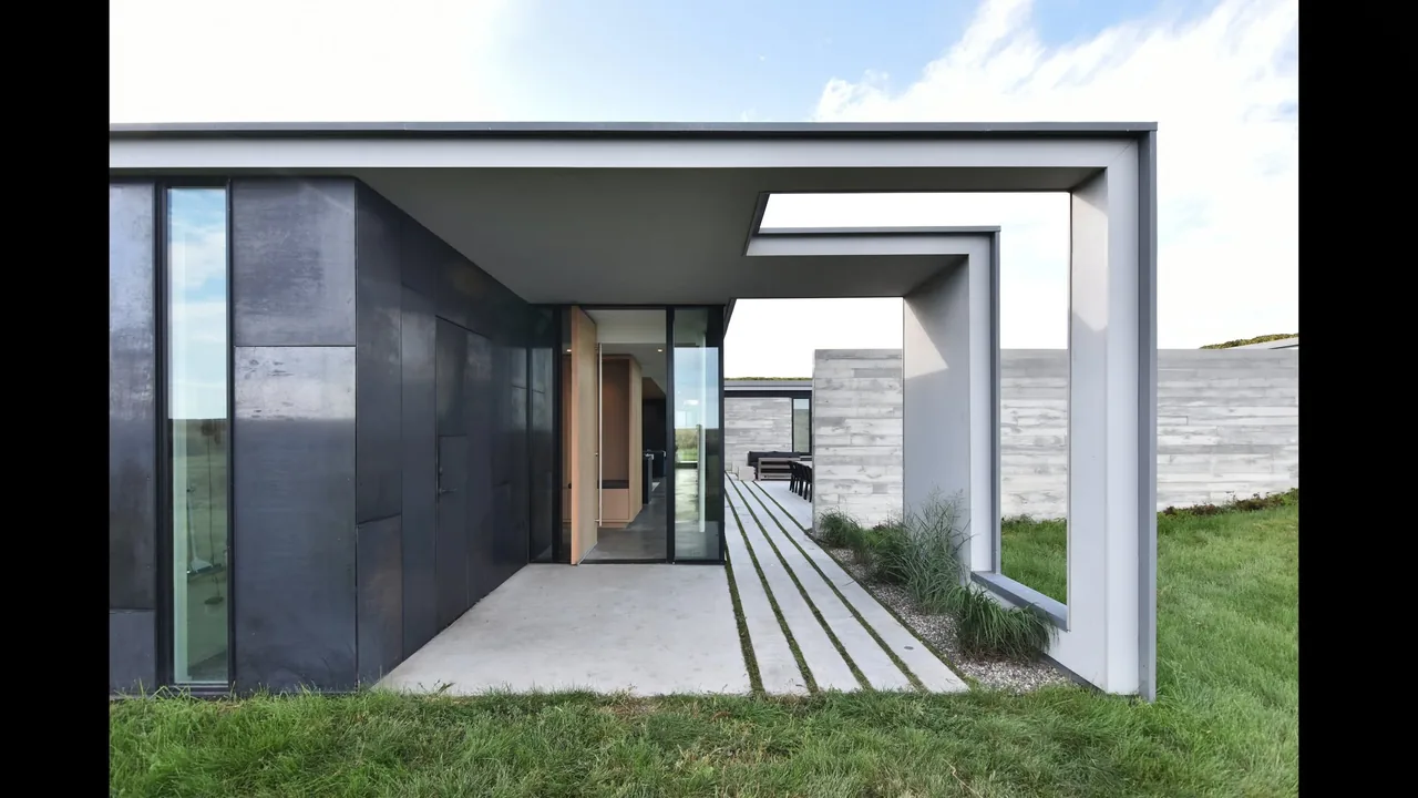 Modern house entrance with black metal cladding, glass walls, and framed concrete walkway at Spoonbill Ranch.