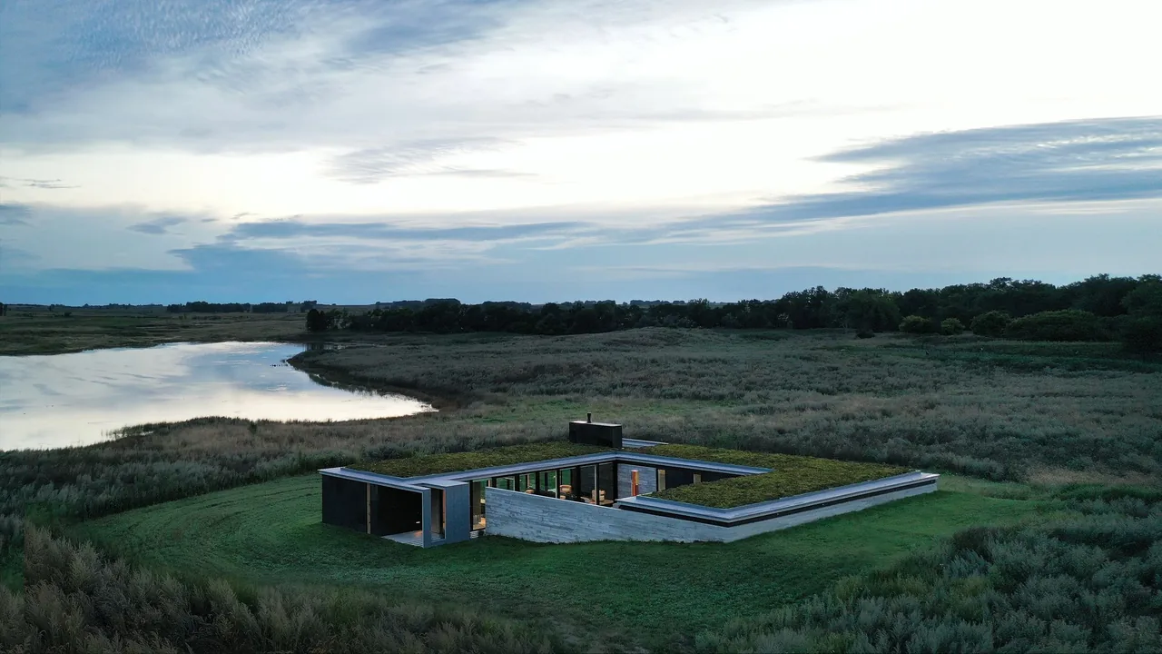 Spoonbill Ranch features a single-story, L-shaped modern home with a green roof overlooking a pond and open landscape.