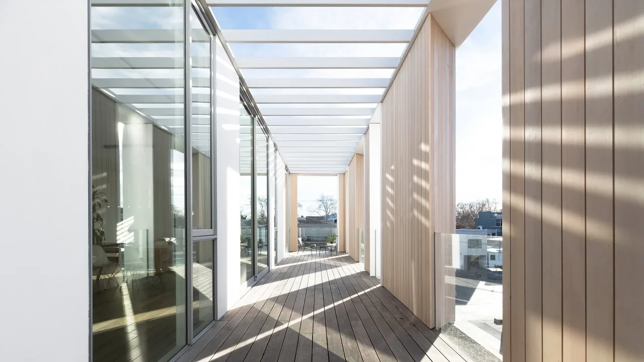 Covered outdoor walkway with glass roof and wood decking in a multi-story urban setting.