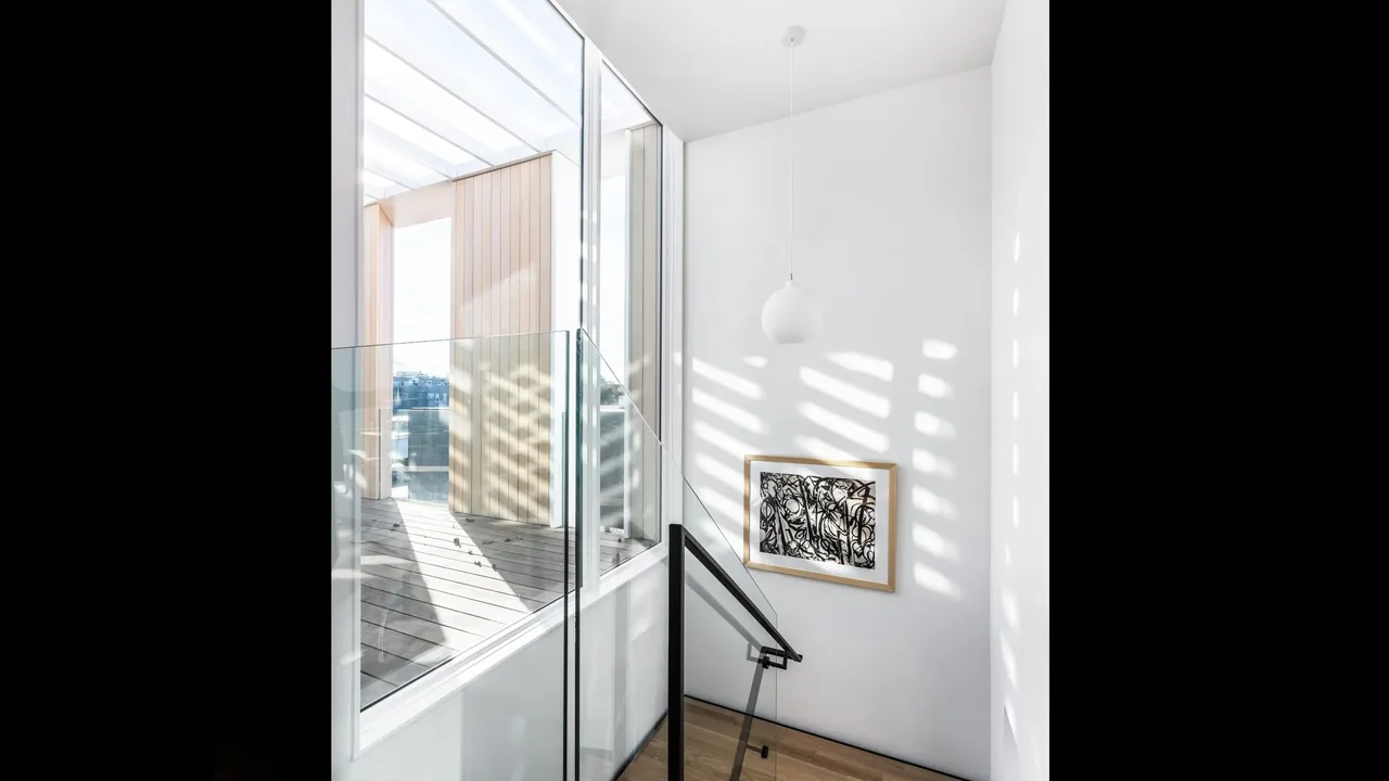 Stairwell with glass railing and pendant light next to a large window opening onto a wood deck with vertical wood siding.