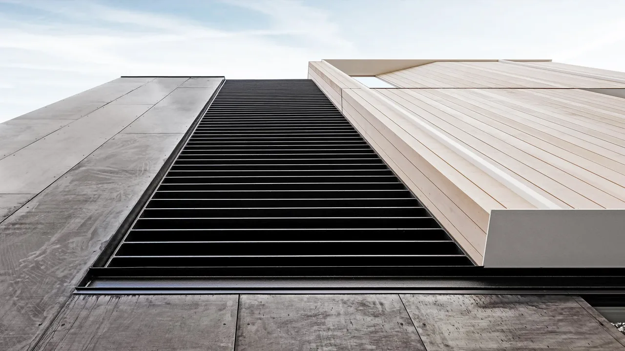 Facade detail of a modern multi-story house showing contrast between vertical wood siding and dark horizontal metal slats.