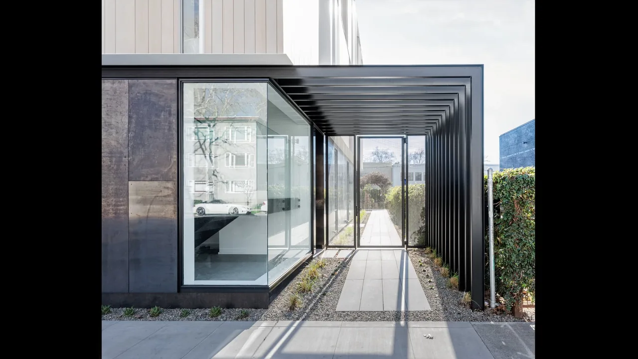 Side exterior of Flex House showing a covered pathway with black metal framework and floor-to-ceiling glazing.