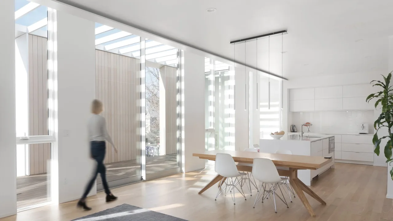 Modern dining area with a wooden table, white chairs, and large floor-to-ceiling glass doors opening to an outdoor space.