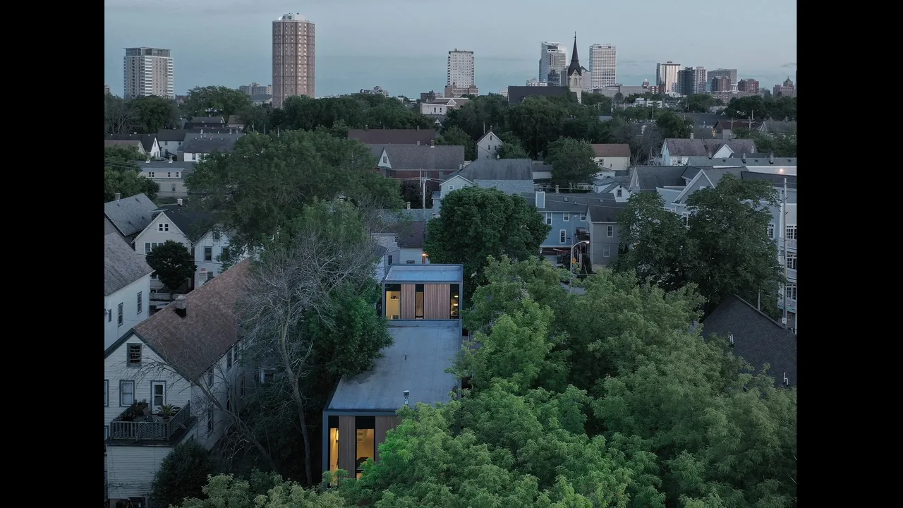 Curtain House by Johnsen Schmaling Architects features a flat roof, vertical wood slat accents, and narrow windows in an urban setting.
