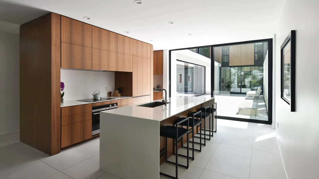 Kitchen features wood cabinetry, a white island with sink, black-framed sliding glass doors leading to a patio.