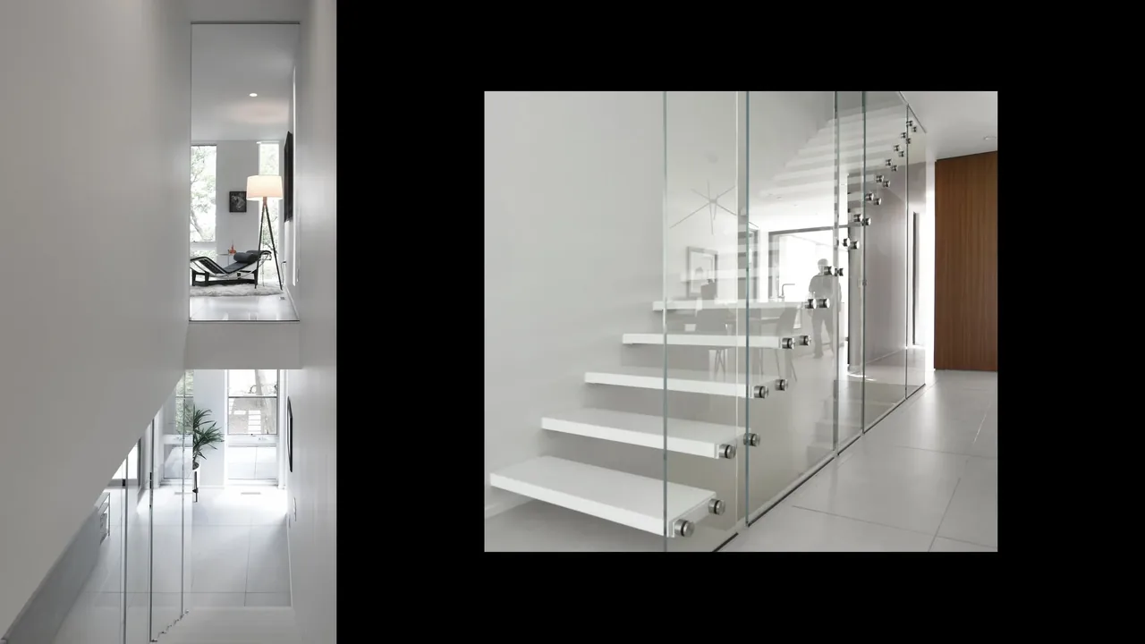 Floating staircase with glass railing in a minimalist home hallway leading to kitchen area.