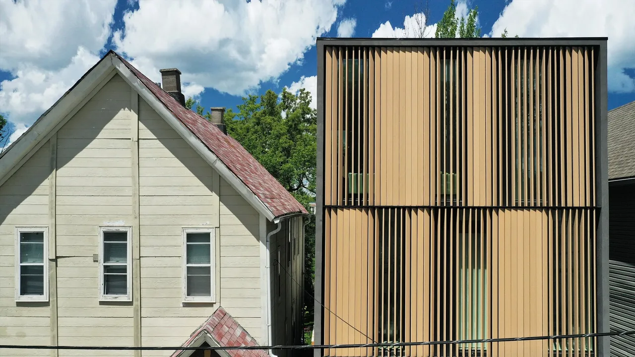Comparison of a traditional pitched roof house and a modern three-story home with vertical wooden slats on the facade.