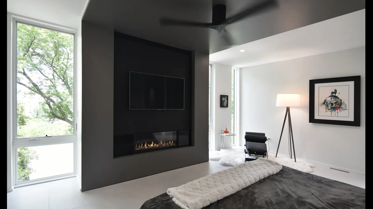 Living room with a black built-in fireplace and wall-mounted TV, accented by tall windows and minimalist furnishings.