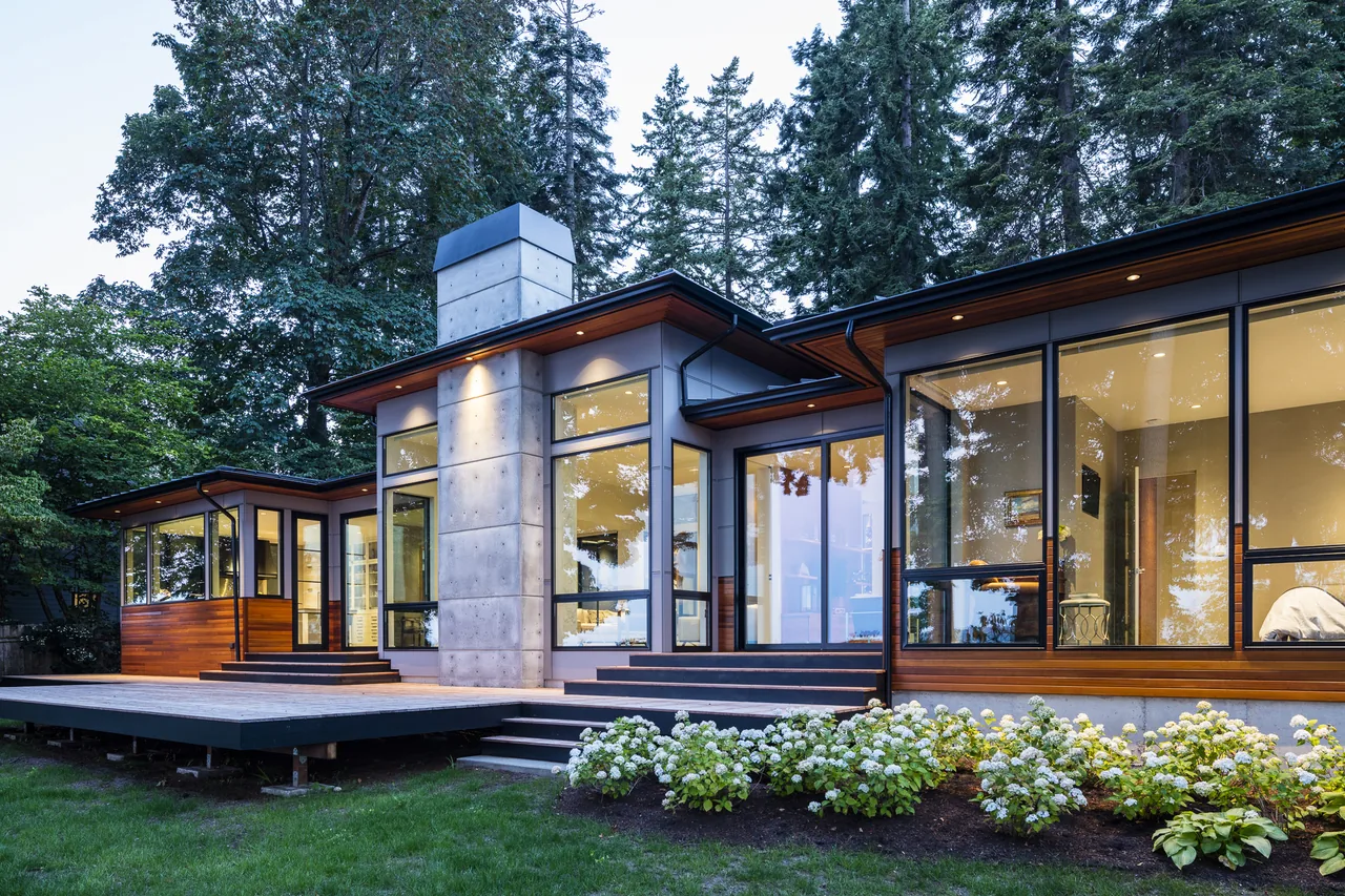 The Sunrise House features extensive floor-to-ceiling glazing, wood siding, and a board-formed concrete chimney, designed by Johnson Squared Architecture + Planning in Seattle.