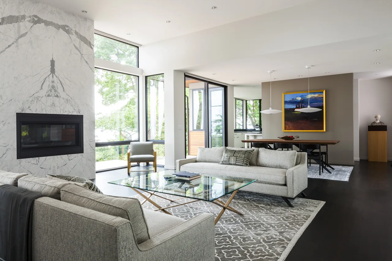 Living room featuring floor-to-ceiling glazing with views of a forested area and a modern fireplace set in a marble surround.