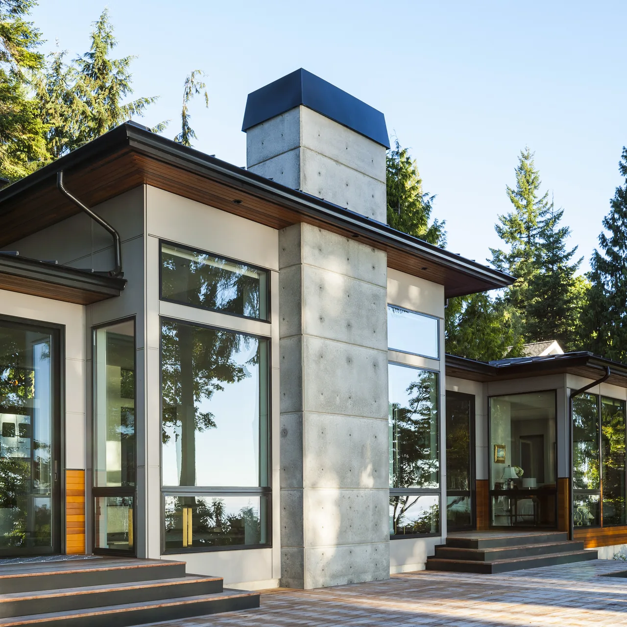 Exterior front view of a modern-style house featuring a concrete chimney and extensive floor-to-ceiling glazing.